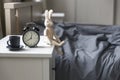 Image alarm clock with a black cup of coffee on white bedside table in front of the bed with gray linens. The room is in beige Royalty Free Stock Photo