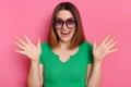 Image of amazed pleasantly surprised girl with brown hair wearing green casual t shirt and sunglasses posing against pink wall,