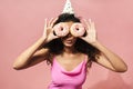 Image of amusing african american woman making fun with donuts