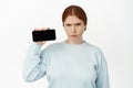 Image of angry frowning redhead girl showing smartphone screen. Ginger woman hold her mobile phone horizontal position Royalty Free Stock Photo