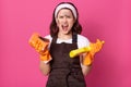 Image of angry tired model posing isolated over pink background in studio, keeps mouth opened, doing household chores, wearing