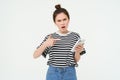 Image of angry young woman complains, points at telephone and looks disappointed, isolated against white background Royalty Free Stock Photo