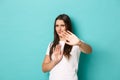 Image of annoyed brunette woman in white t-shirt, defending herself, raising hands to protect eyes from bright light Royalty Free Stock Photo