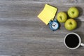 An image of apples, cup of coffee, alarm clock, stickers lying on a wooden table