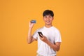 Image Asian man with credit card and a mobile phone on orange background