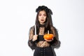Image of asian woman panicking, being scared of witchcraft on halloween, standing in witch costume with candle and Royalty Free Stock Photo