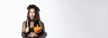 Image of asian woman in wicked witch costume, looking left serious, holding lit candle and pumpkin, celebrating