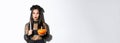 Image of asian woman in wicked witch costume, looking left serious, holding lit candle and pumpkin, celebrating