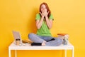 Image of astonished teenage girl screaming while studying with exercise books, lap top, pens, coffee. Surprised student sitting at Royalty Free Stock Photo