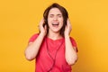 Image of attractive energetic brunette wearing casual red t shirt, having headphones, listening to music, singing, enjoying