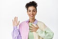 Image of attractive queer girl raising hand, holding hand on chest, introduce herself, volunteering, making promise Royalty Free Stock Photo