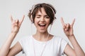 Image of attractive woman in basic t-shirt showing rock sign while listening to music with headphones Royalty Free Stock Photo