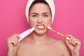 Image of attractive woman with dark hair, holding toothbrushe and tooth paste in hands, has angry facial expression, female