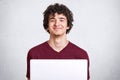 Image of attractive young guy with curly hair wearing casual maroon t shirt, sitting in front of open laptop, looking smiling Royalty Free Stock Photo