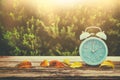 Image of autumn Time Change. Fall back concept. Dry leaves and vintage alarm Clock on wooden table