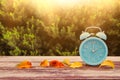 Image of autumn Time Change. Fall back concept. Dry leaves and vintage alarm Clock on wooden table outdoors at afternoon