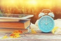 Image of autumn Time Change. Fall back concept. Dry leaves and vintage alarm Clock on wooden table outdoors at afternoon