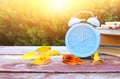 Image of autumn Time Change. Fall back concept. Dry leaves and vintage alarm Clock on wooden table