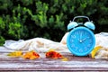 Image of autumn Time Change. Fall back concept. Dry leaves and vintage alarm Clock on wooden table