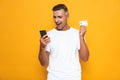 Image of bearded guy 30s in white t-shirt holding mobile phone and credit card Royalty Free Stock Photo