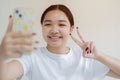 Image of beautiful Asian girl laughing and showing peace sign while taking selfie photo on cellphone Royalty Free Stock Photo