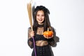 Image of beautiful asian woman dressed-up as a witch for halloween party, holding broom and pumpkin, standing over white Royalty Free Stock Photo