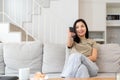 Image of a beautiful asian woman searching channel with remote control to watch tv while sitting on sofa at home Royalty Free Stock Photo