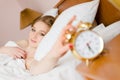 Image of beautiful blond young business woman blue eyes girl touching alarm clock off wake up time looking at camera happy smiling Royalty Free Stock Photo