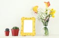 Image of beautiful bouquet of yellow spring flowers next to blank vintage photo frame over white table. For photography mock up mo