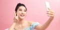 Image of beautiful brunette woman laughing and showing peace sign while taking selfie photo on cellphone  over pink Royalty Free Stock Photo