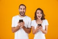 Image of beautiful couple man and woman smiling while both using mobile phones, isolated over yellow background Royalty Free Stock Photo