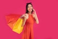 Image of a beautiful excited happy asian woman posing isolated over pink wall background holding shopping bags talking by mobile Royalty Free Stock Photo