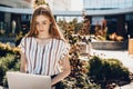 Beautiful ginger girl with freckles using a computer outside sitting on a bench in the city near a lot of flowers Royalty Free Stock Photo