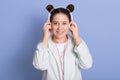 Image of beautiful girl with double buns hairstyle looking directly at camera while listening to music via headphones isolated Royalty Free Stock Photo