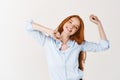 Image of beautiful girl with long red hair snap fingers and dancing, enjoying listening music, standing against white