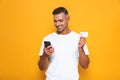 Image of beautiful guy 30s in white t-shirt holding mobile phone and credit card Royalty Free Stock Photo