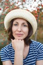 Image of beautiful middle-aged woman wearing straw hat laughing and looking at camera while walking in summer park Royalty Free Stock Photo