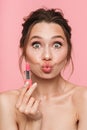 Shocked happy young woman posing isolated over pink wall background holding lipstick Royalty Free Stock Photo