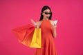 Image of a beautiful shocked young asian woman posing isolated over pink wall background holding shopping bags using mobile phone