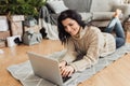 Image of beautiful smiling young woman shopping online on laptop in cozy Christmas interior. Female lying on the floor next the Royalty Free Stock Photo