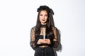 Image of beautiful woman celebrating halloween in witch costume, holding candle and squinting at camera suspicious