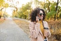 African happy woman walking outdoors in a spring park drinking coffee talking by mobile phone Royalty Free Stock Photo