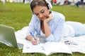 Young pretty woman in park outdoors using laptop computer listening music writing notes.