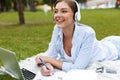 Young pretty woman in park outdoors using laptop computer listening music writing notes. Royalty Free Stock Photo