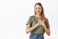Image of beautiful young woman holding hands on heart, smiling and looking pleased flattered, receive heartfelt surprise