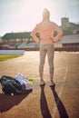 Image from behind of caucasian young female standing at the athletic track with hands on hips, preparing for training, visualizing