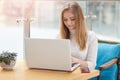 Image of blonde charming girl dressed white casual shirt, works with laptop in cafeteria, woman looks concentrated at conpurer