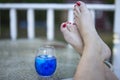 Image of a blue cocktail on a porch table with a woman`s barefoot chilling out beside the drink. Royalty Free Stock Photo