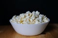 Image of a bowl of freshly-popped popcorn placed on a table, with a soft focus background