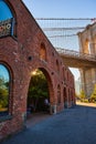 Brick building with arches and golden sun peeking through next to stunning iconic Brooklyn Bridge in New York City